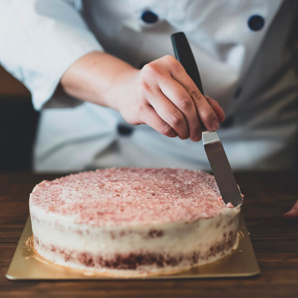 Eine Torte wird mit der Winkelpalette dekoriert. Die Bäckerin zieht damit feine Linien in die Sahne.